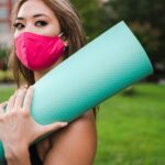 Woman walking outdoors with protective face mask and yoga mat