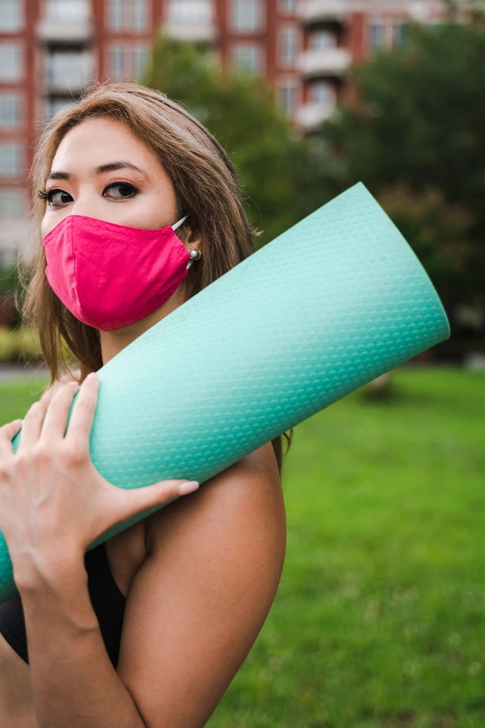 Woman walking outdoors with protective face mask and yoga mat